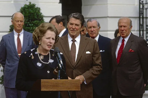 margaret-thatcher-discursando-em-um-microfone-ao-lado-de-ronald-reagan-atras-deles-outros-politicos
